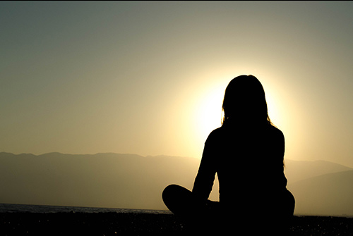 A person meditating at sunrise